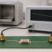 Single two-terminal MLCC in a measurement fixture with a completed thermal-history backdrop and a conceptual slow downward time trend