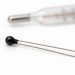 Unbranded black bead NTC thermistor with a blurred thermometer on a white background